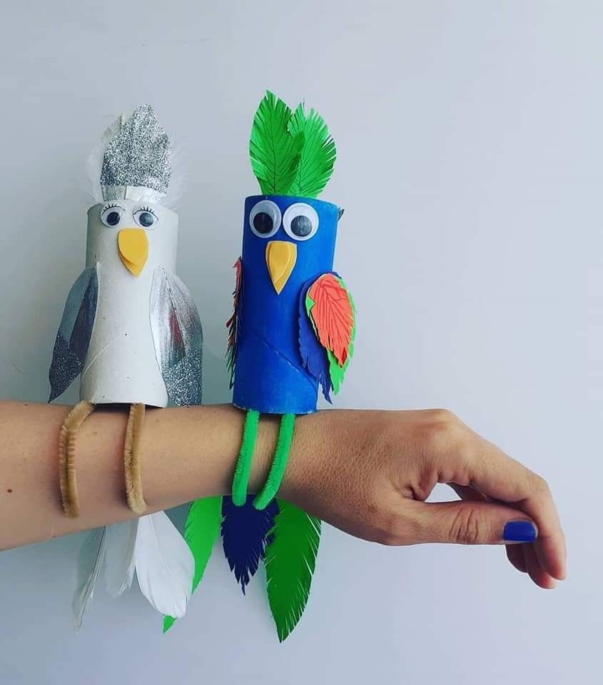 Two colorful handmade parrot crafts resting on a person arm made from tubes and paper