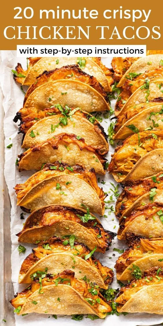 Mini baked crispy chicken tacos on parchment paper with melted cheese, shredded chicken, and fresh cilantro garnish