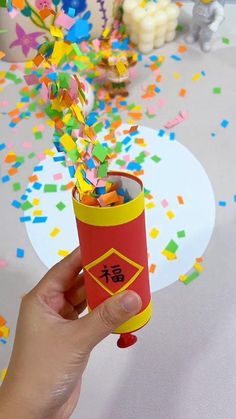 Hand holding a handmade red and yellow festive confetti popper with a balloon base surrounded by colorful confetti.