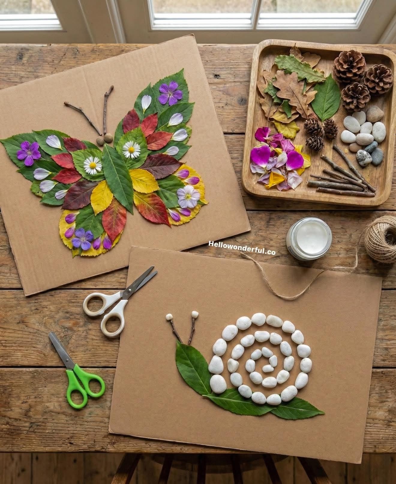A wooden table displaying a nature collage butterfly and a snail craft made from leaves, flowers, and stones on cardboard.