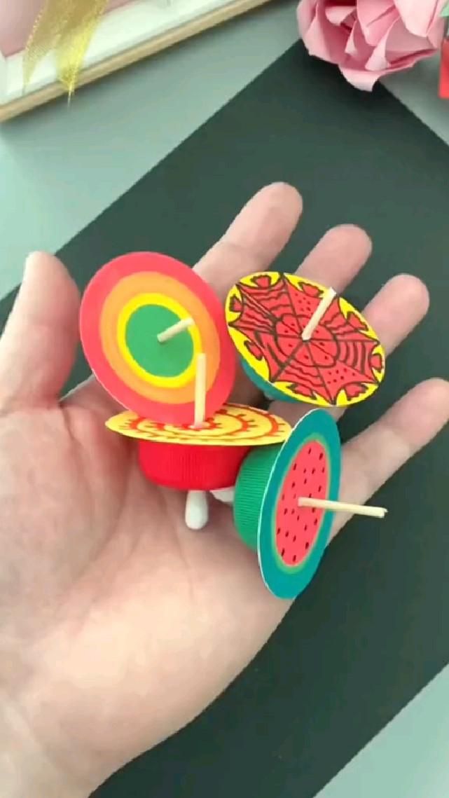 Hand holding colorful DIY paper spinners with toothpick axles and designs like a spiderweb and watermelon.