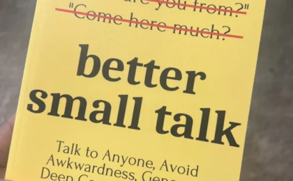 Hand holding yellow paperback titled Better Small Talk by Patrick King, with crossed-out cliché conversation starters