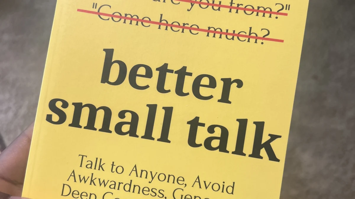 Hand holding yellow paperback titled Better Small Talk by Patrick King, with crossed-out cliché conversation starters