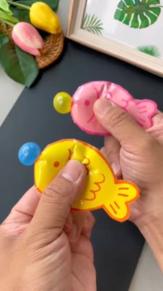 Hands squeezing colorful pink and yellow goldfish paper crafts that feature small bubbles coming out of their mouths.