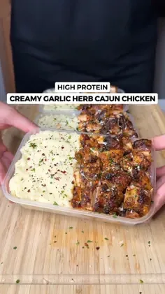 Two meal prep containers with creamy Cajun chicken and mashed potatoes on a wooden board