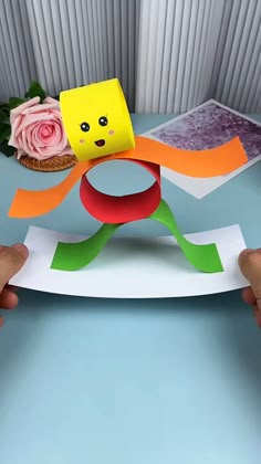 Colorful handmade paper craft of a dancing person with a yellow head and red body held on a blue surface