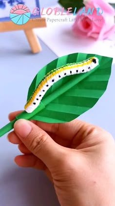 A green paper caterpillar toy wiggling on a flat surface with accordion-folded body segments