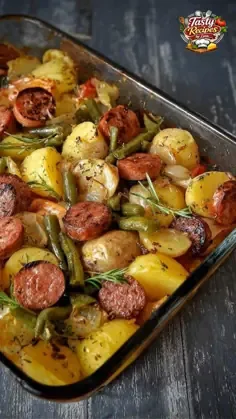 Baking dish with sliced smoked sausage, potato wedges, green beans, caramelized onions, rosemary sprigs, and melted cheese.