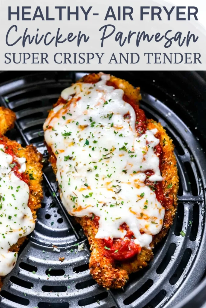 Two golden-crispy air-fried chicken breasts topped with red sauce, melted mozzarella, and parsley in a black air fryer.