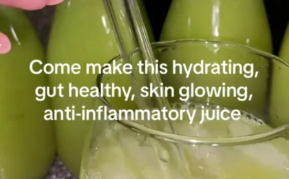 A tall glass of vibrant hydrating green juice surrounded by fresh cucumber, celery, green apple, and leafy greens on a light.