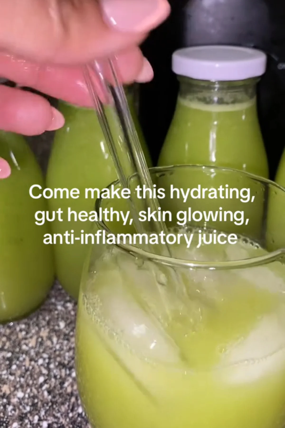 A tall glass of vibrant hydrating green juice surrounded by fresh cucumber, celery, green apple, and leafy greens on a light.