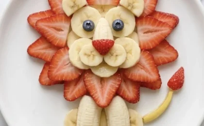Colorful lion-shaped fruit salad on a round plate with mango slices for a mane, blueberries for eyes and nose, and a.