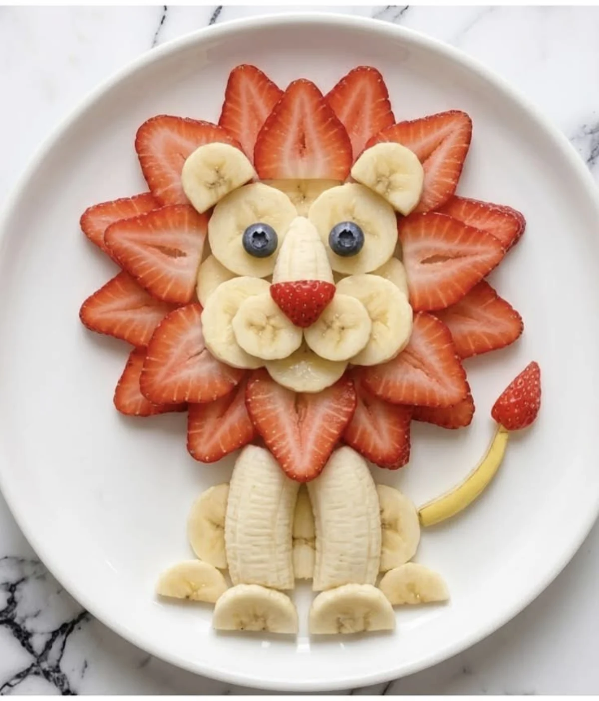 Colorful lion-shaped fruit salad on a round plate with mango slices for a mane, blueberries for eyes and nose, and a.