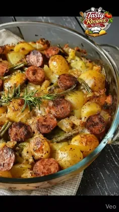 Glass baking dish with roasted potatoes, sliced smoked sausage, green beans, melted cheddar cheese, and fresh rosemary.