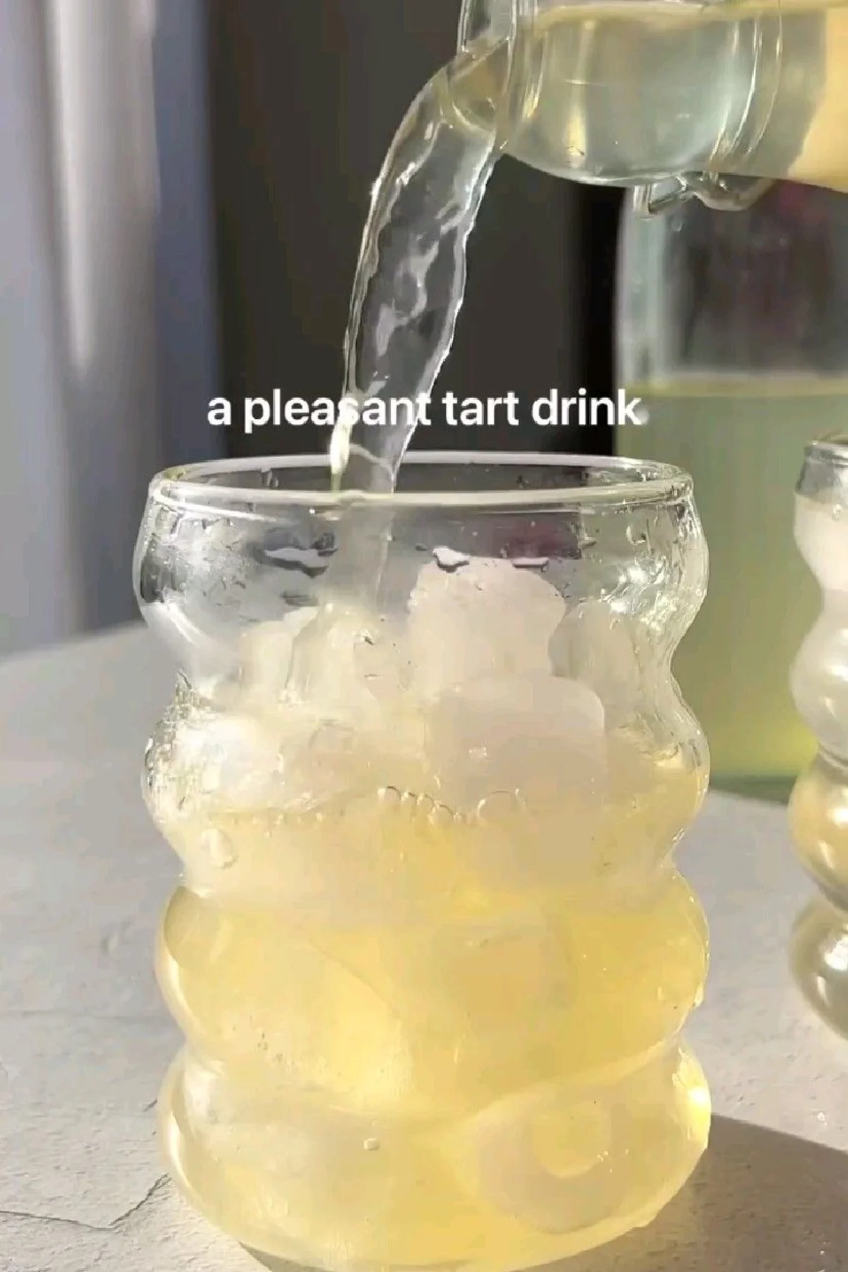 A clear pitcher of infused ginger lemon water surrounded by fresh lemons, sliced ginger root, and vibrant mint on a light.