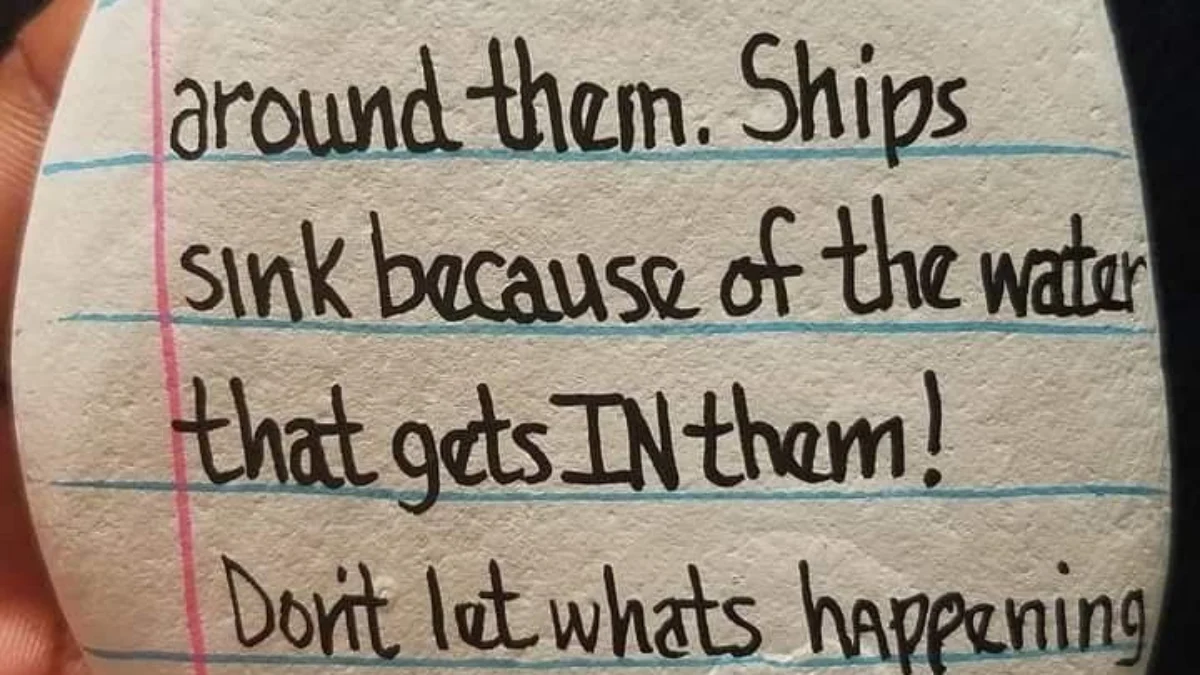 Hand holding a smooth stone painted with the motivational message Ships don’t sink because of the water around them Isaiah.