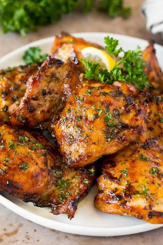 Golden-brown umami marinated boneless skinless chicken thighs on a white plate with parsley and lemon garnish.