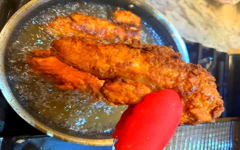 Golden crispy chicken tenders frying in a hot skillet with bubbling oil