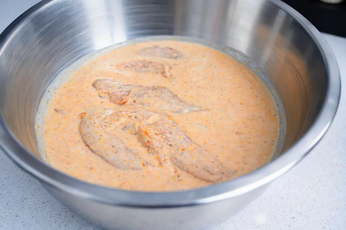 Chicken tenderloins soaking in buttermilk batter mixture in a large metal bowl