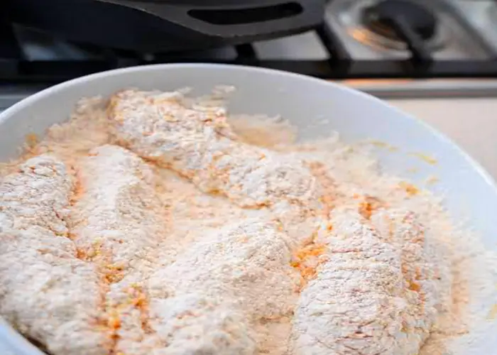 Raw chicken tenderloins seasoned with spices in a blue bowl ready for marinating