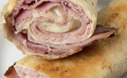 Golden air-fried ham and Swiss cheese roll cut in half on a white plate