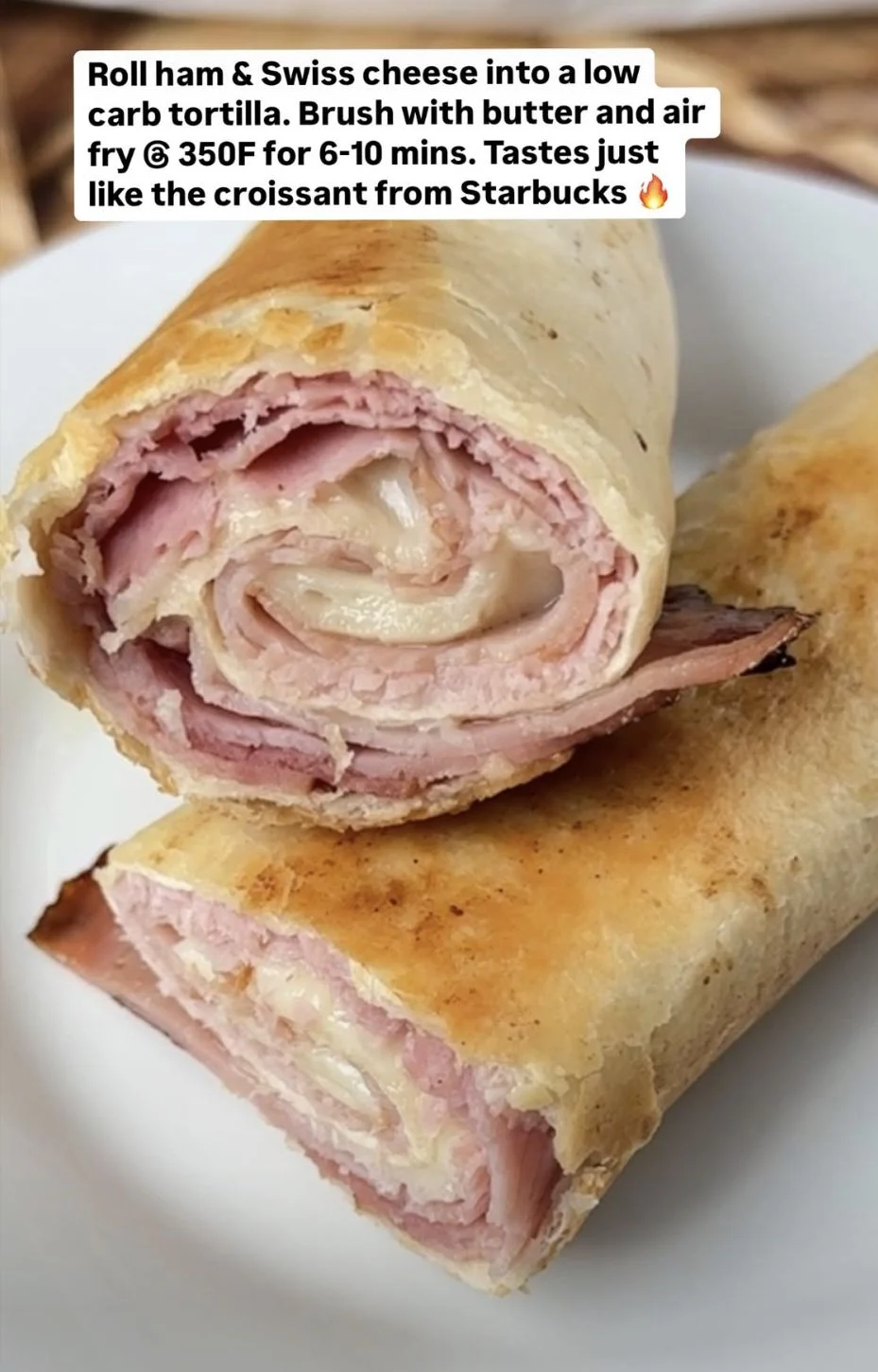 Golden air-fried ham and Swiss cheese roll cut in half on a white plate