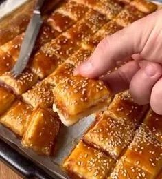 Golden-brown cheese and ham pinwheels on a parchment-lined baking sheet, one being separated with a knife