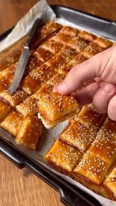Golden-brown cheese and ham pinwheels on a parchment-lined baking sheet, one being separated with a knife