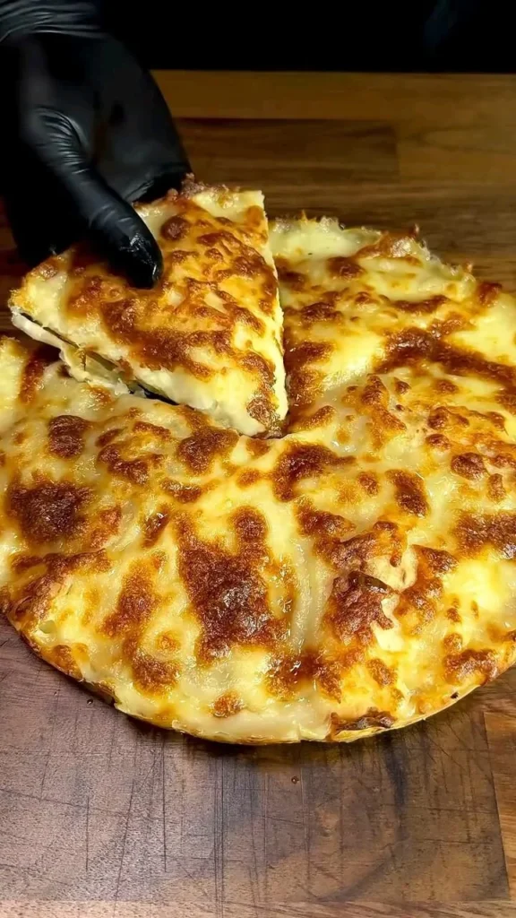 Golden brown cheese and spinach pie on a wooden board with one slice removed