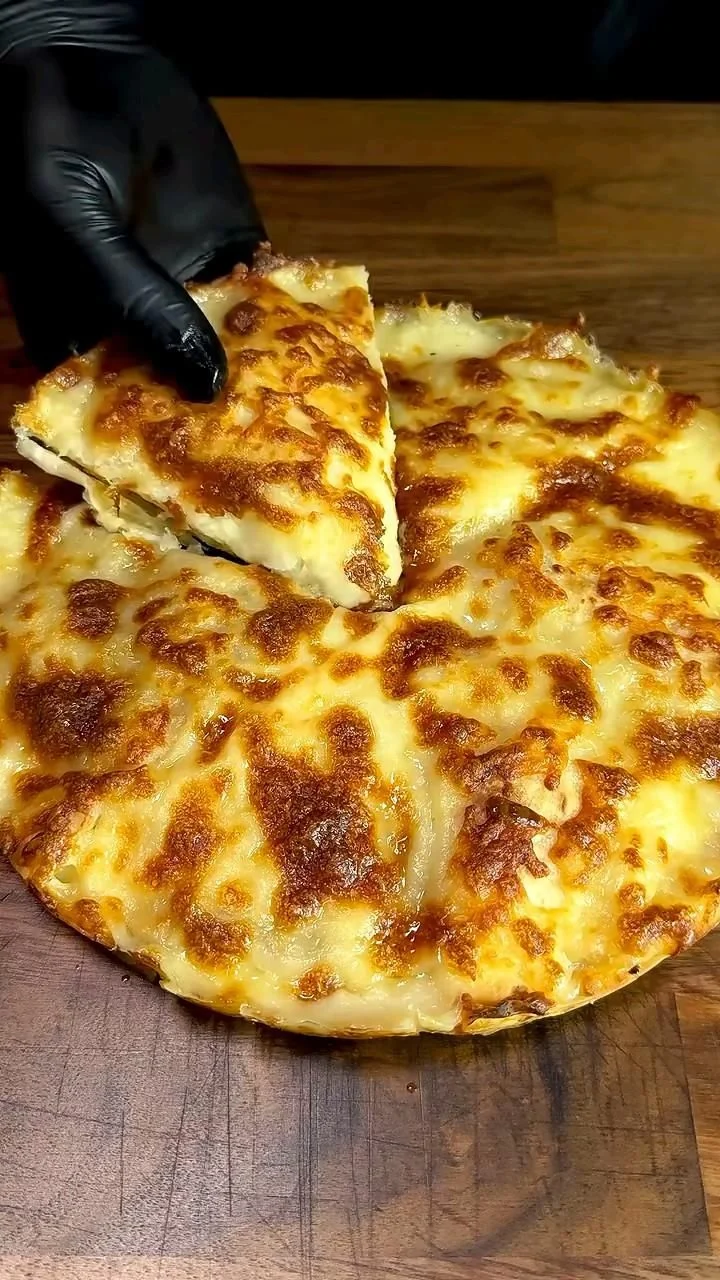 Golden brown cheese and spinach pie on a wooden board with one slice removed