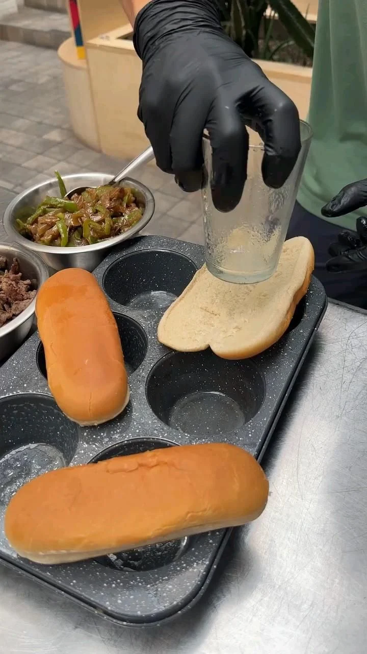 Assembling a Philly cheesesteak with cheese on a hoagie roll in a muffin tin