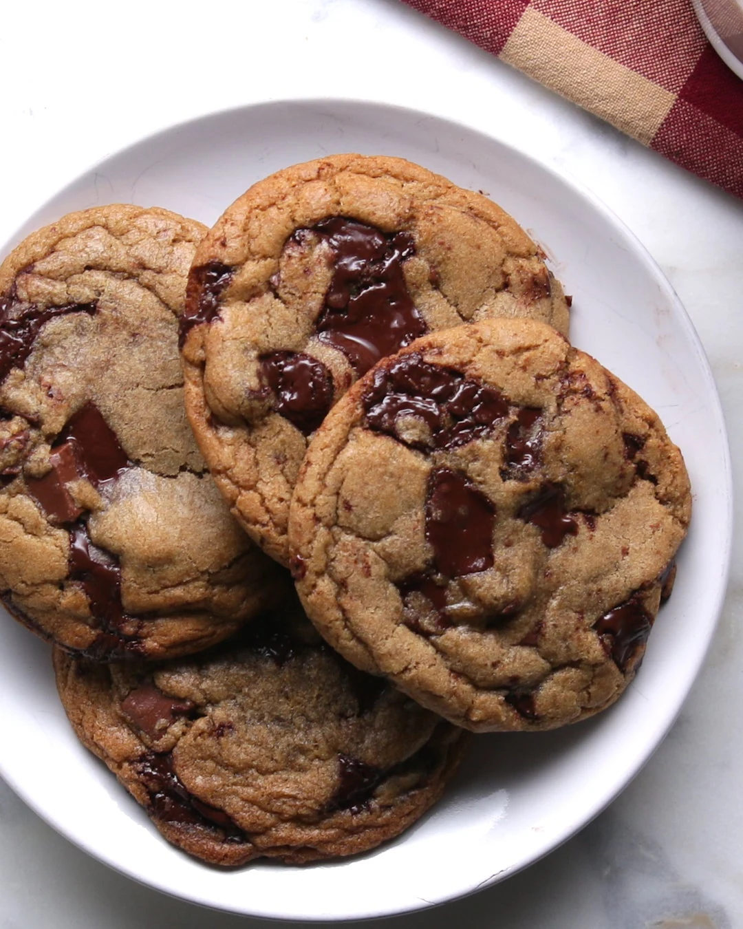 Golden brown chewy chocolate chip cookies with large dark chocolate pieces on a white plate