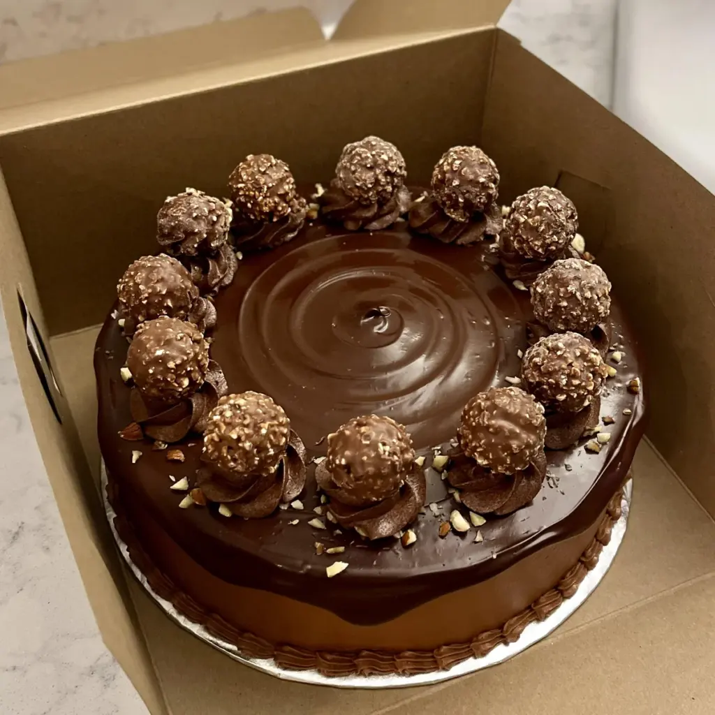 A tall chocolate layer cake topped with piped ganache swirls and a Ferrero Rocher chocolate, inspired by the famous hazelnut treat.