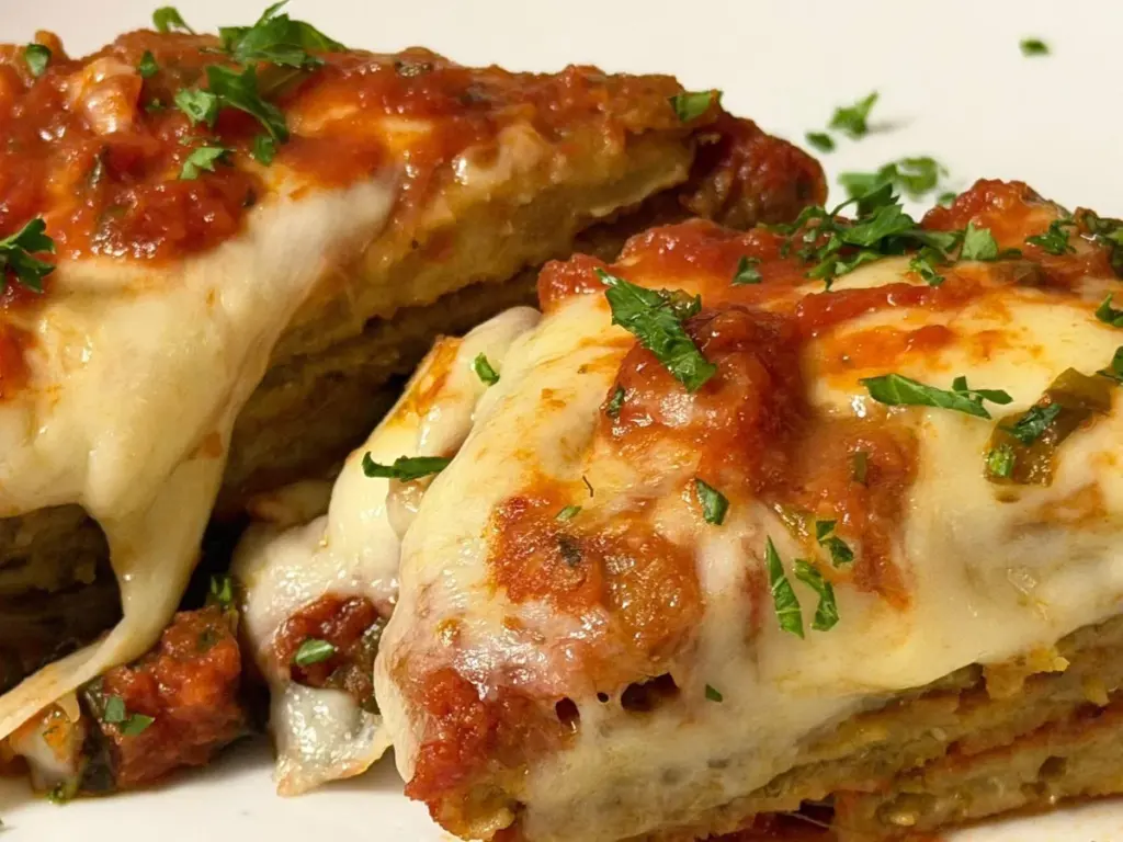 A golden-brown baked eggplant parmesan in a rectangular glass baking dish, topped with melted cheese and tomato sauce, with a spatula lifting a serving.