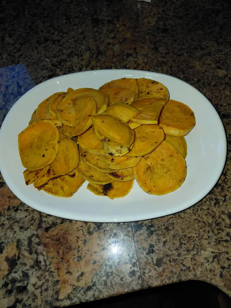 Golden roasted sweet potato slices on a foil-lined baking sheet, seasoned with olive oil, salt, sage, and pepper.