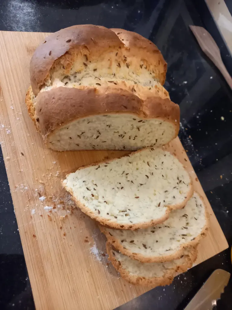 A rustic round loaf of cumin bread with a golden-brown crust, sitting on a wooden cutting board.